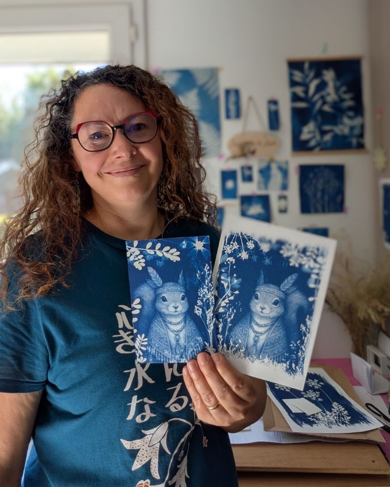 Marie-Cécile, artisane créatrice de cyanotypes, tenant deux cartes faites main dans son atelier Les Paillettes by Pepite